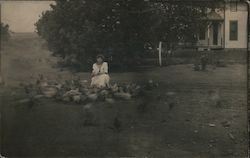 Woman in white dress feeding several dozen birds near house Postcard