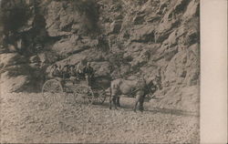 Portrait of group sitting in simple horse-drawn wagon. Rocky landscape. Postcard