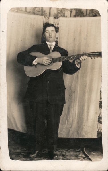 Man with a Guitar Playing in Front of a Sheet Backdrop