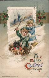 A boy and girl with a doll sliding down a hill on a sled - A Merry Christmas to you Postcard