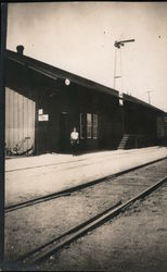 Man Standing Between Train Tracks and Station Postcard