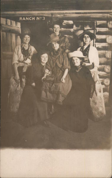 A Group of Women Wearing Hats Sitting in Front of a Log Cabin