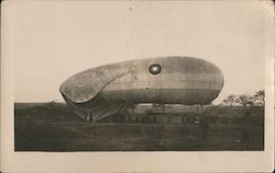 Blimp in field with people holding ropes Postcard