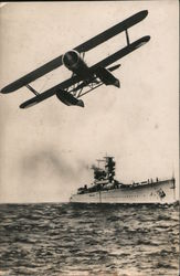 One engine biplane with battleship in background Postcard