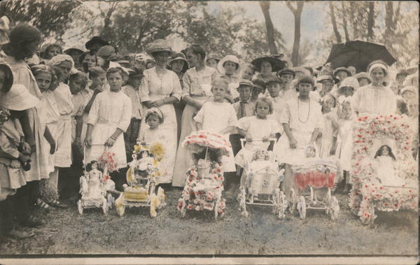 Group of people dressed in white, and girls with flowered doll strollers