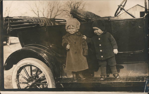 Two small children wearing hats, standing in a parked car.