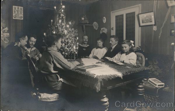 Family gathered around Christmas tree on table. Three sailors and family