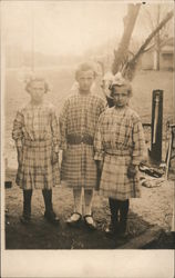 Three young girls with bows in hair and plaid dresses Postcard