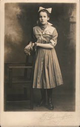 Girl with dress and hairbow, posing by chair Postcard