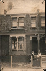 Two women pose by a gate in front of a building Postcard