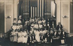 Group of people posing in front of organ pipes and a flag Postcard