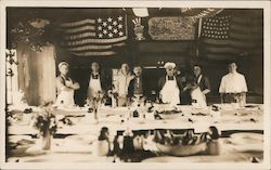 Group of people, some in aprons and chef hats, posing in front of a table Postcard