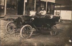 Man - and dog - sitting in car in front of building Postcard