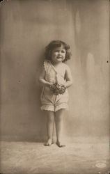 Little girl in white top and bloomers, holding flowers Postcard