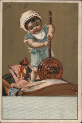Baby playing with toys in cradle by Maxyne Barense Trade Card