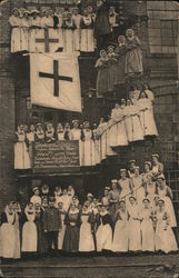 Red Cross nurses posed on outside building stairwells under large Red Cross Flag. Postcard