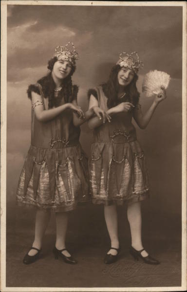 Studio Photo of two girls identical dress, crowns, one has feather fan
