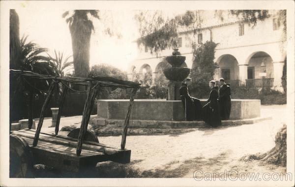 Monks sitting by a fountain in front of a mission church