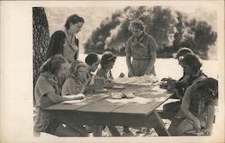 Girl Scout troop doing arts and crafts under tree on bench Postcard