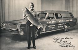 Harold Ensley, station wagon with logos Ford Show. Harold holding large fish. Signed Postcard