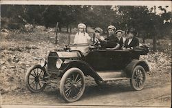 People riding in car, dirt road, Ford Model T Postcard