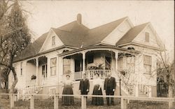 Family posing outside a wooden house with a porch Postcard