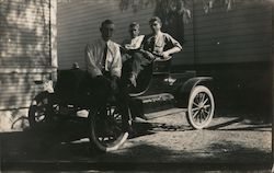 Three men sitting in open car in yard under shade of tree Postcard