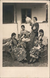 Four women outside a building, wearing traditional dress, working on crafts Postcard