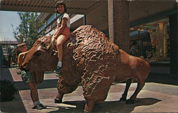 Bison - Two girls climb on a bison sculpture on the Mall at The Landing Kansas City Missouri