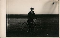 Man with a bicycle standing in a field Postcard