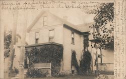 Two-story wooden house with ivy-covered front porch, ivy growing over windows Postcard