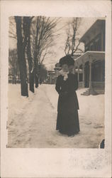 Woman dressed in black stands on snowy residential street Postcard