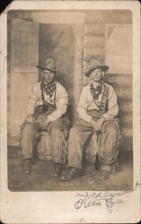 Two Men dressed as Cowboys outside a Log Building Postcard