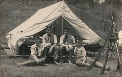 4 Young US soldiers posed in front of a tent, with stacked rifles nearby. Postcard