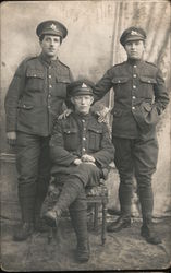 Three soldiers posing for photo, two are standing, one is sitting. Postcard