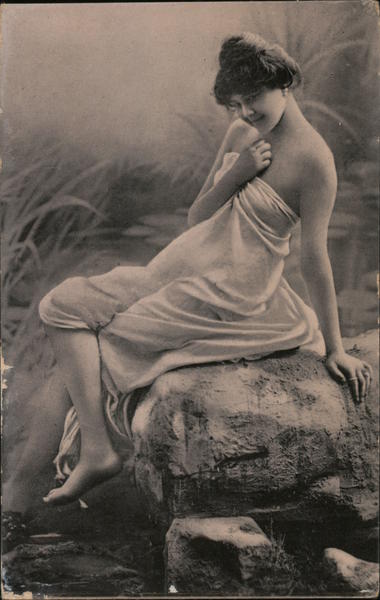 Young woman wrapped in a white cloth is reclining on a rock over a river